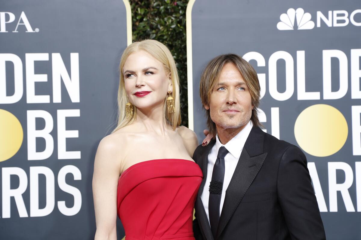 Nicole Kidman in a red strapless dress, looking over her shoulder as she poses next to Keith Urban in a suit