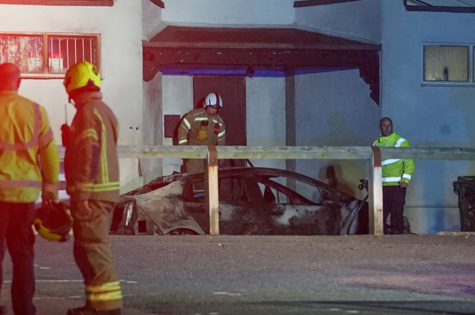 Firefighters and a security guard stand outside Peachaven Mosque where an arson attack destroyed a car.