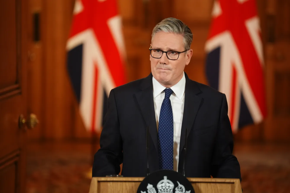 Keir Starmer at a podium with two Union Jack flags in the background.