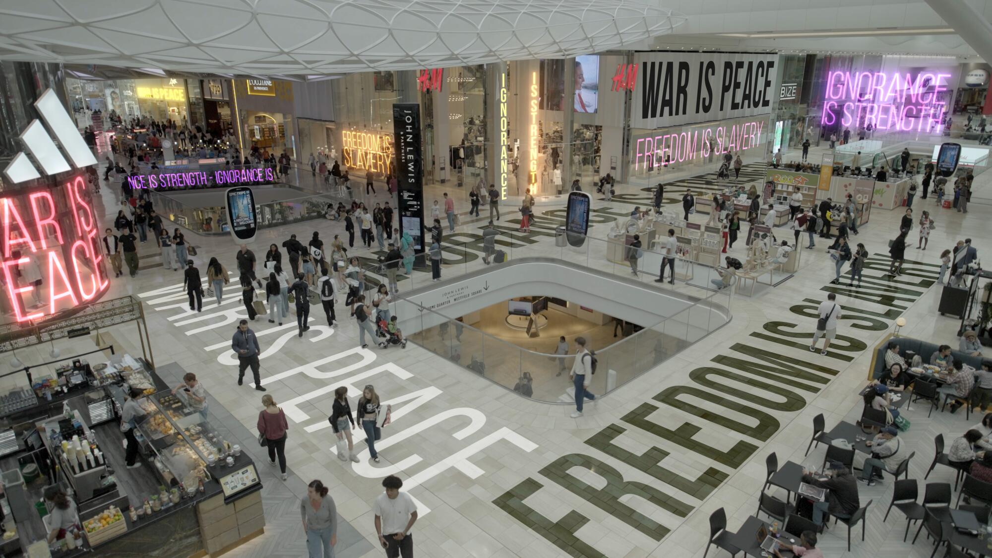 People shop in a busy mall with Orwellian signage underfoot.