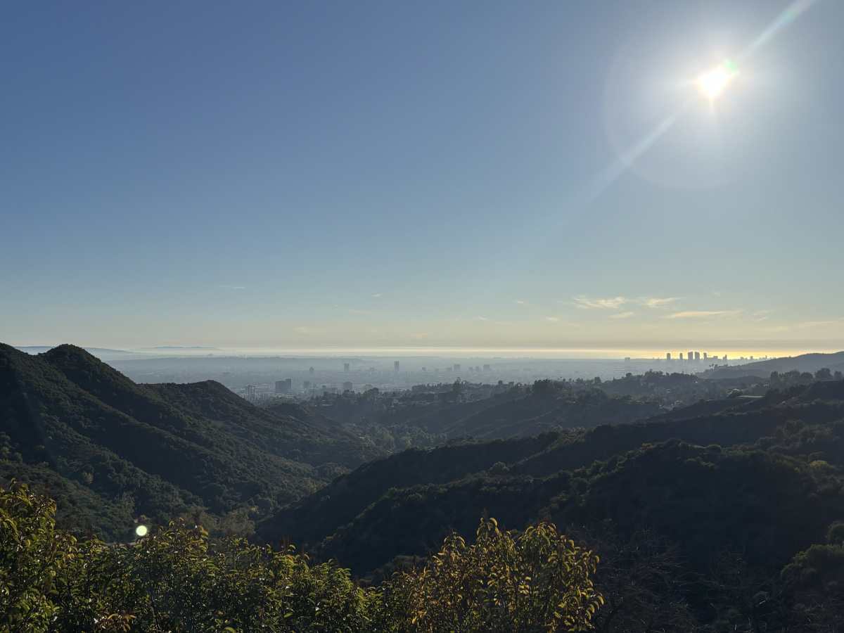 Rolling green mountains and hills in the foreground with an outline of downtown L.A. in the background.