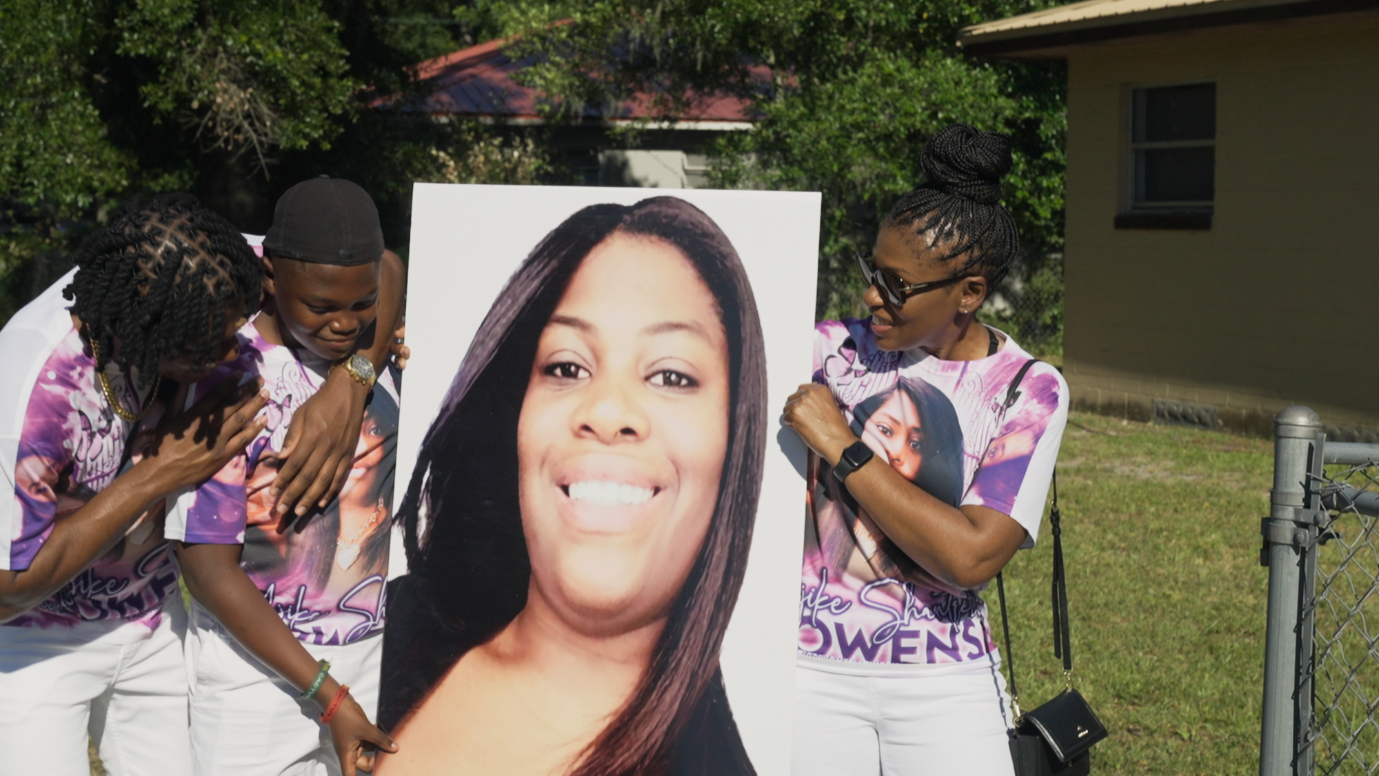 Three people hold up a picture of a deceased woman at a memorial service.