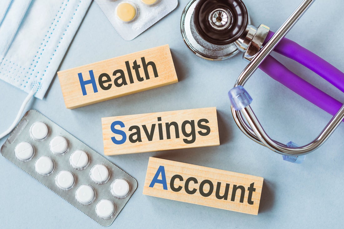 Three wooden blocks reading Health, Savings, and Account, surrounded by a stethoscope and packages of pills.