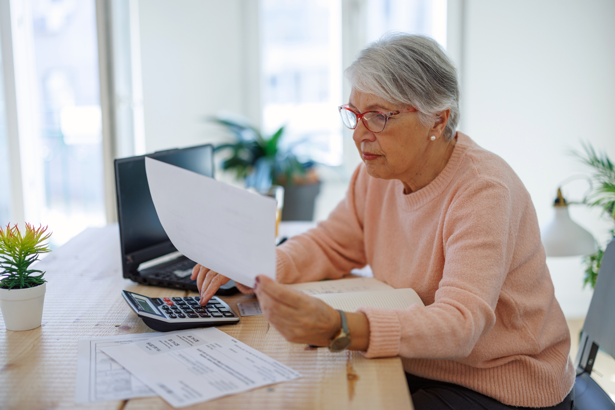 A person holding a document while using a calculator.