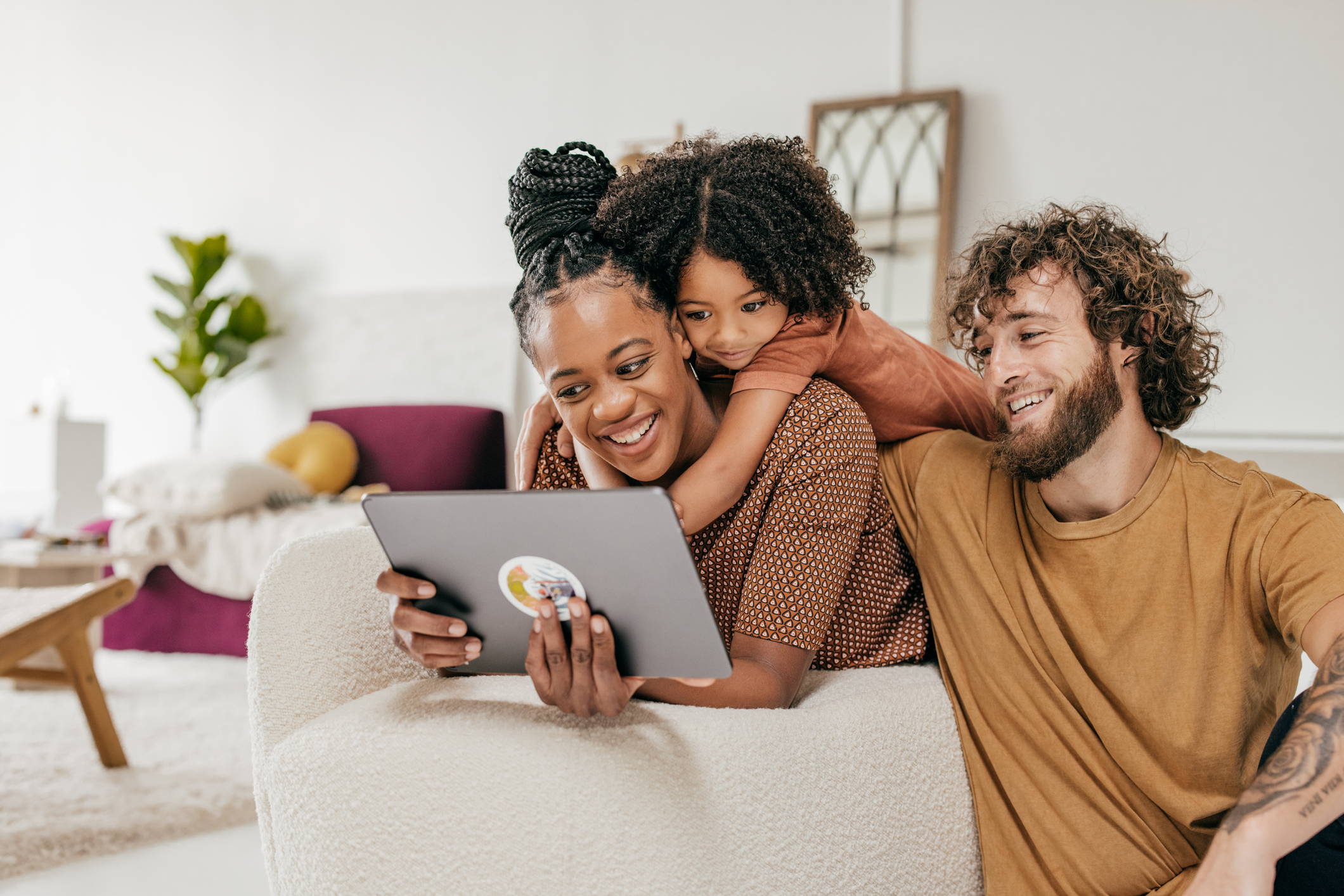 Two adults and a child looking at a tablet and smiling.