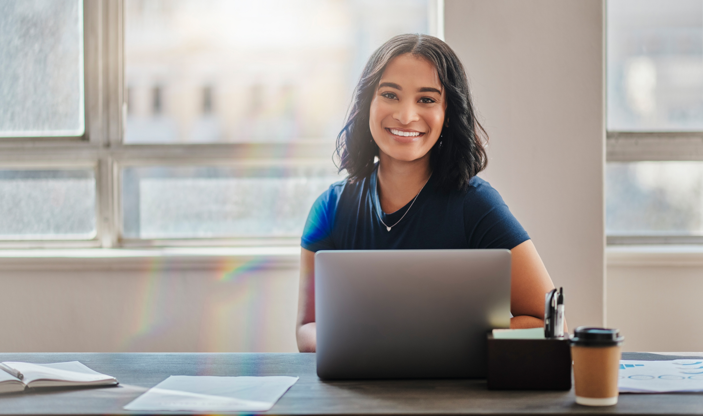 A smiling young person at a laptop.