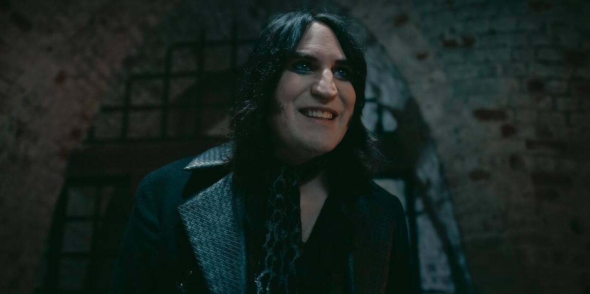 A man with dark hair and dark clothing standing near an arch with iron bars in an old building.