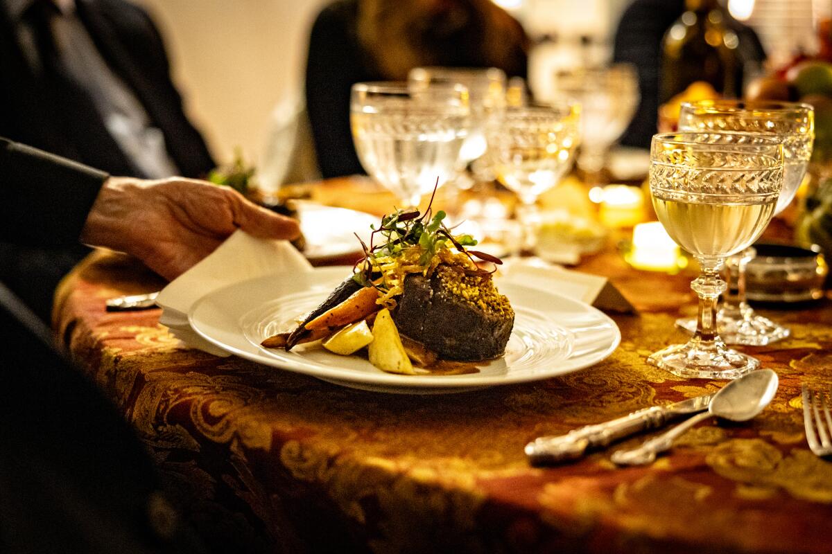 A plate with steak and roasted vegetables sits on a table with glassware. 
