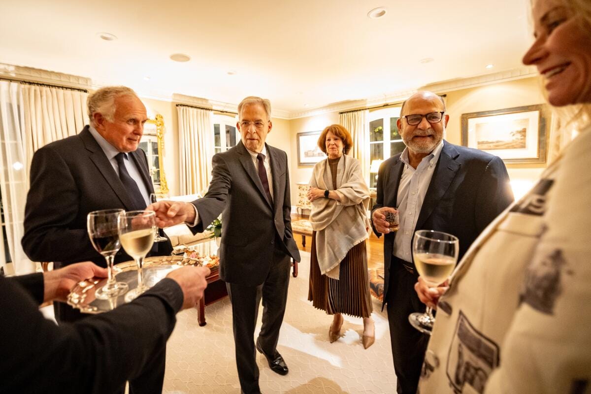 Men and women stand in a living room drinking wine.