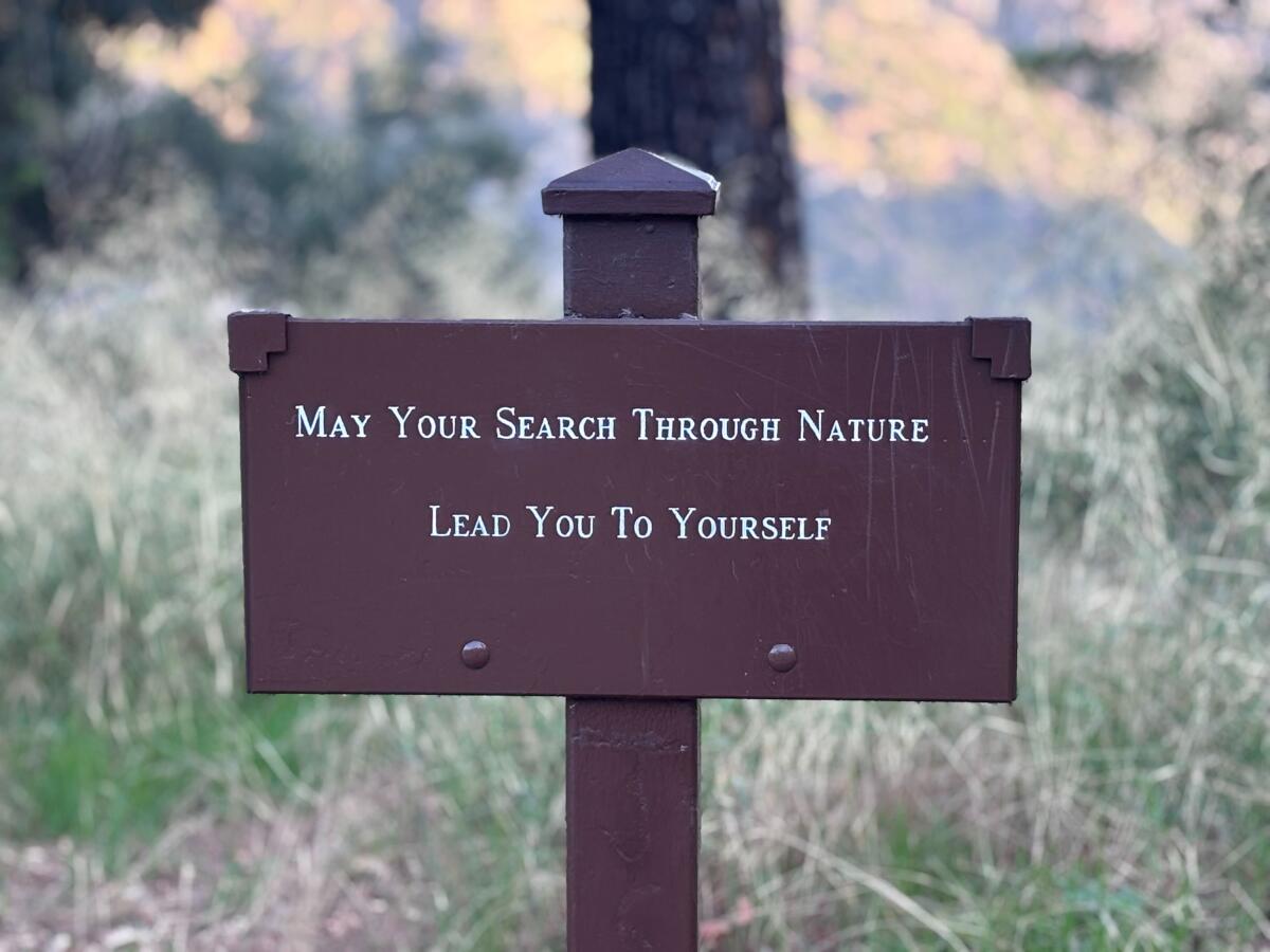 A brown sign near the trail that reads: "May your search through nature lead you to yourself." 