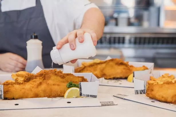 Close up of boxes of fresh fish and chips being seasoned with salt