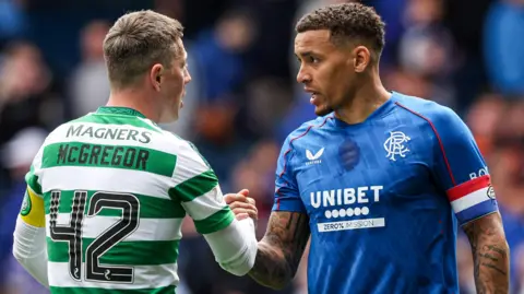SNS Celtic captain Callum McGregor - who is wearing a green and white hooped jersey - and Rangers captain James Tavernier - who is wearing a royal blue jersey - shake hands.