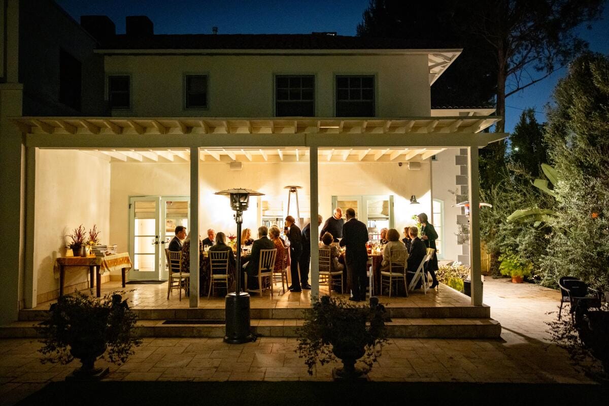 Men and women sit around tables at a back patio.  