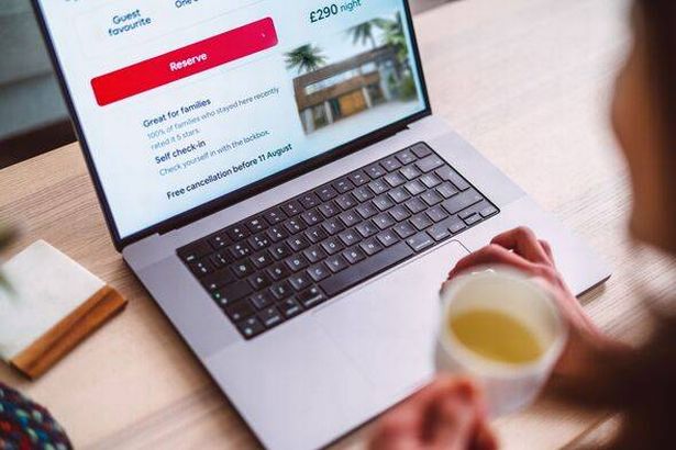 Over the shoulder view of a person booking accommodation on travel app on laptop at home