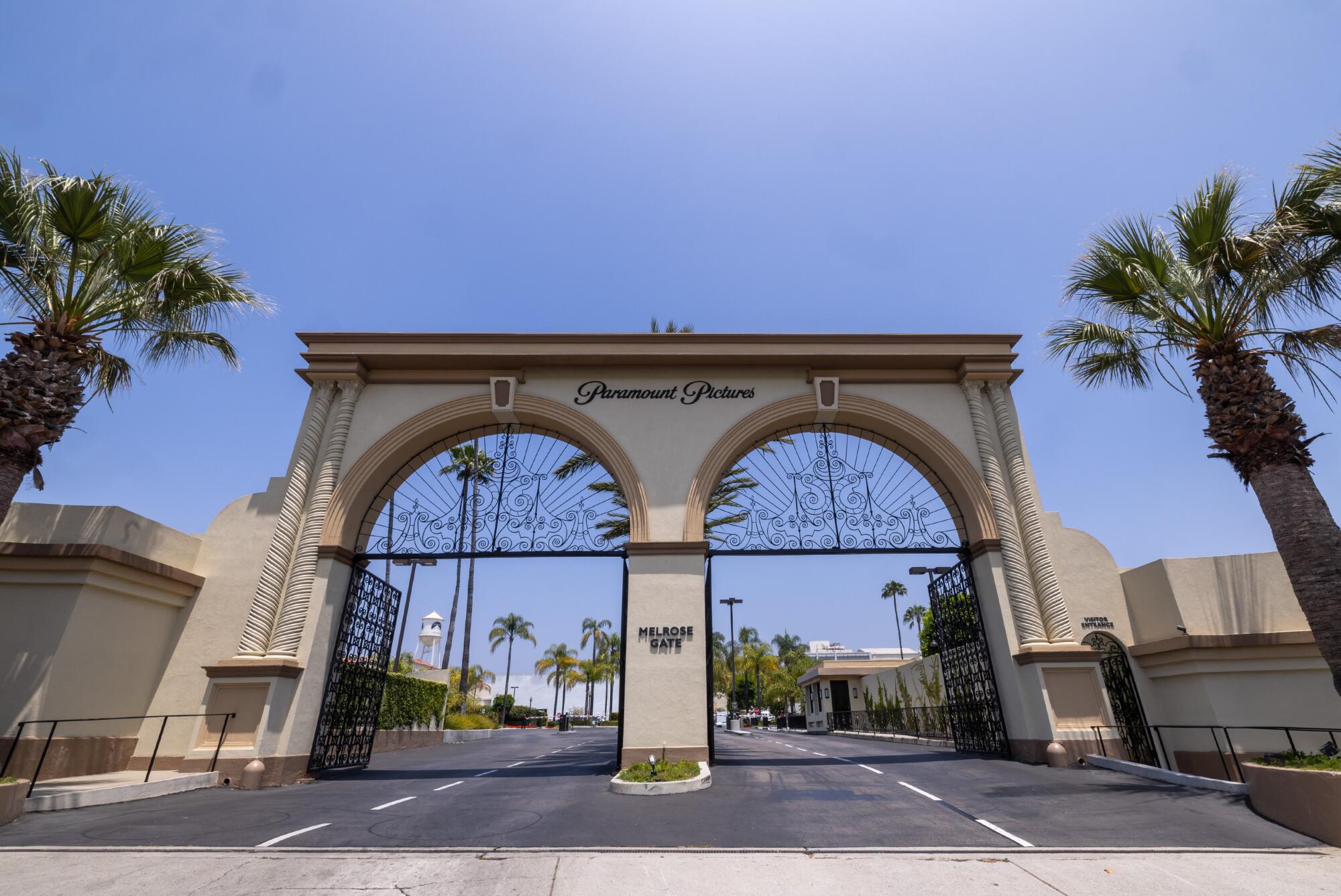 The gate of a studio lot is framed by palm trees.