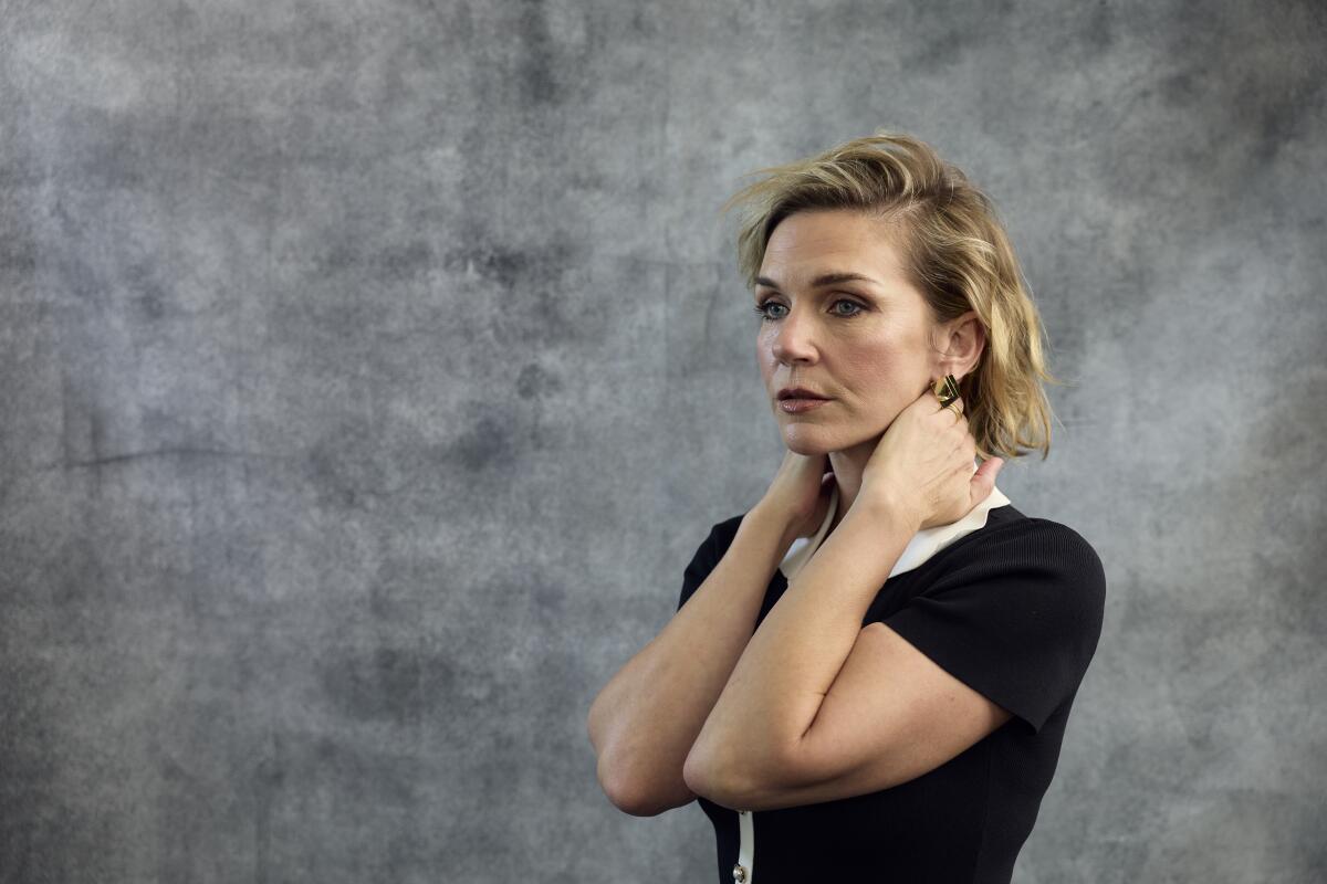 A woman gazes into the distance with both hands raised and clasped around her neck.