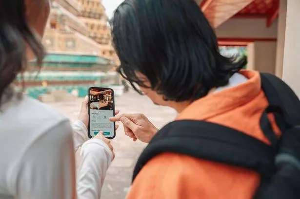 Group of mature adult friends quickly booking a hotel on smartphone while exploring the temple