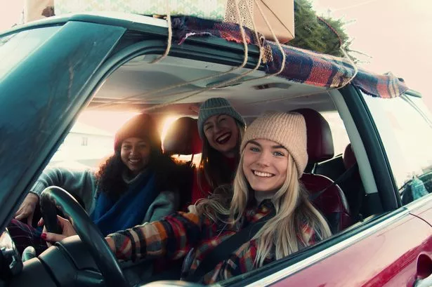 Three happy young excited multiethnic women posing, smiling at camera in fancy red car on snowy winter road slow motion. Festive mood on Christmas celebration, female friends on vacation road trip.