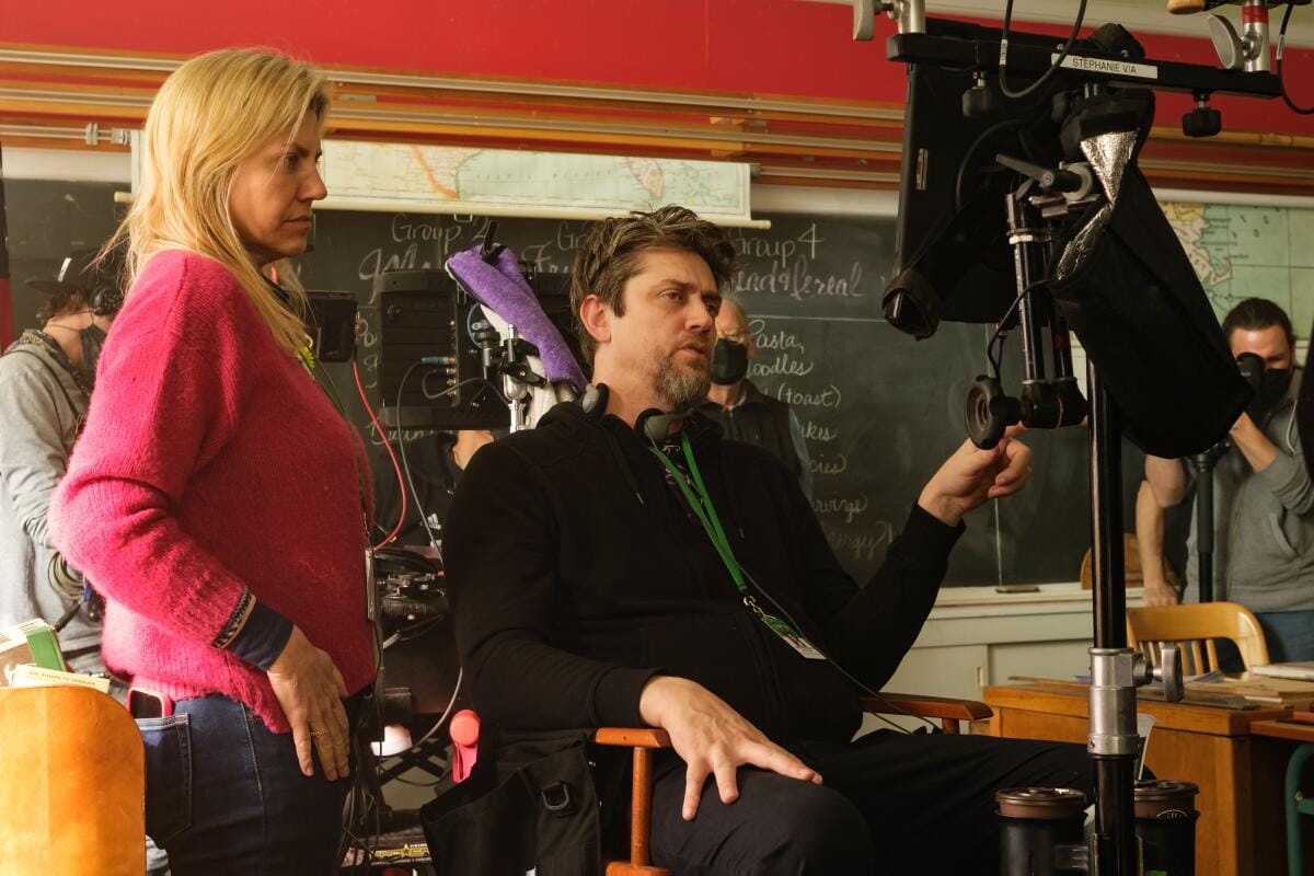 A woman in a pink sweater stands near a man in a black sweater with headphones around his neck looking at a screen.