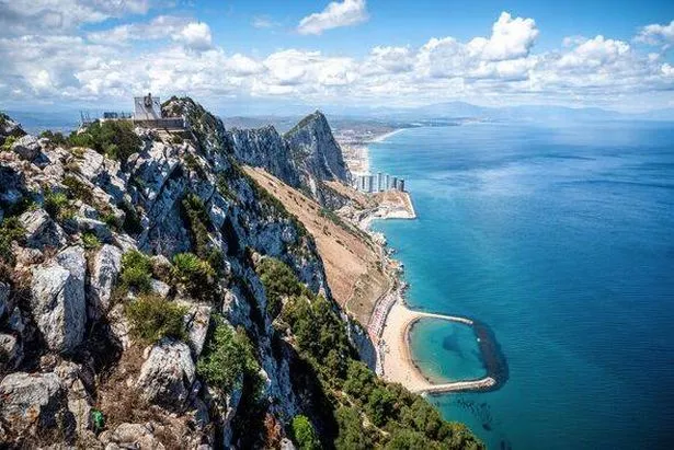 Aerial panorama capturing Gibraltar's dramatic limestone landmark, urban landscape, surrounding azure waters, and hazy African coastline under dramati